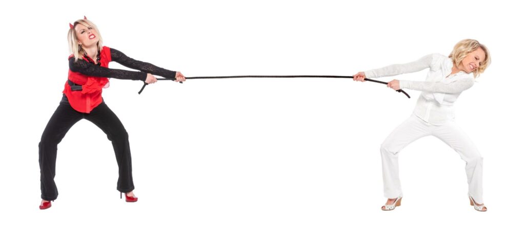 Two women, one dressed as a devil and the other as an angel, engage in a tug-of-war.