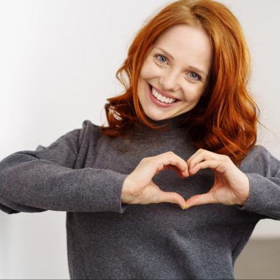 A redhead making a heart shape with her hands, illustrating how acts of service are tied to intention.
